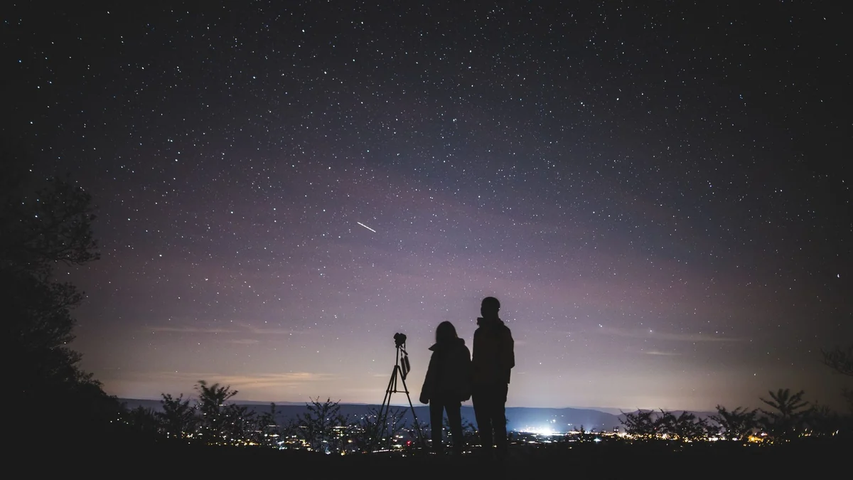 Duas pessoas observando as estrelas sob a Via Láctea